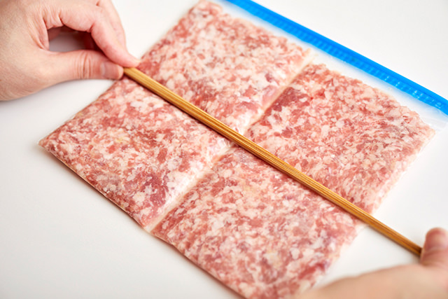 冷凍用密封保存袋に入れた豚挽き肉に菜箸を押しつけている写真