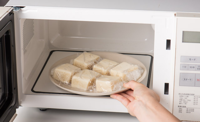 ラップで包んだ冷凍豆腐を電子レンジで解凍する写真