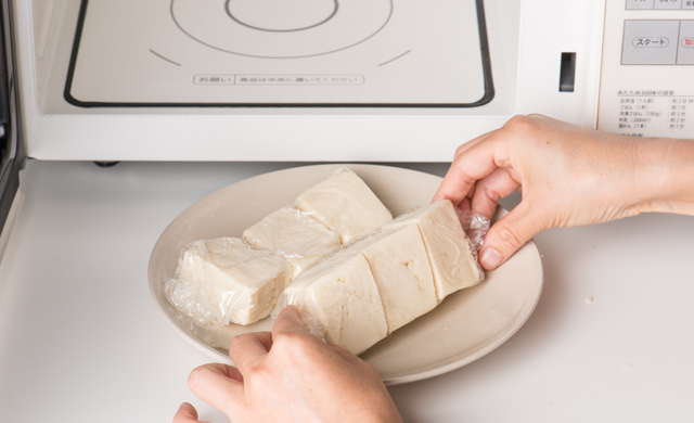 ラップで包んだ冷凍豆腐を電子レンジで解凍する写真