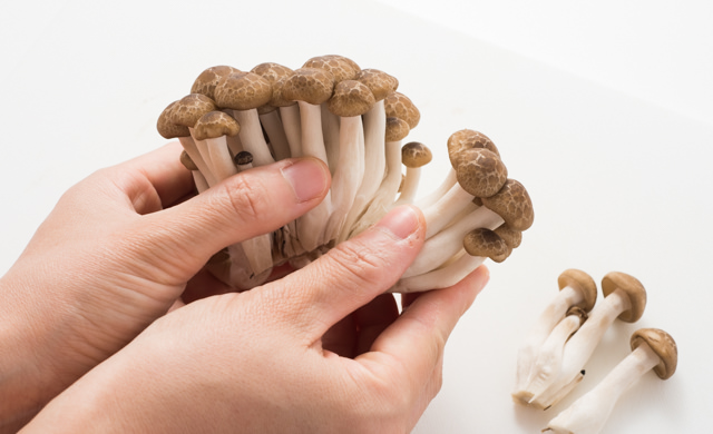 根元を切り落としたしめじを手でほぐしている写真