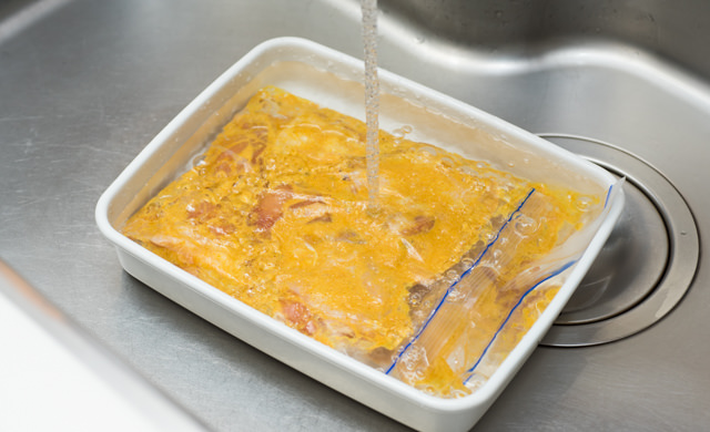 冷凍したタンドリーチキンを流水解凍している写真