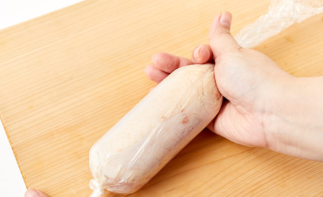 ラップの端を結び、結んだ方に鶏肉を寄せていくところ