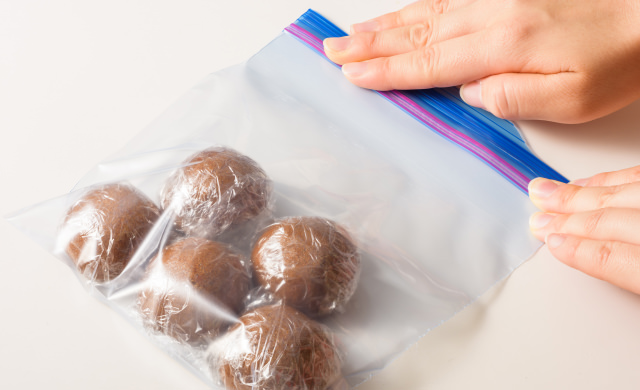 ラップで包んだまんじゅうを冷凍用保存袋に入れ、空気を抜きながら口を閉じている写真