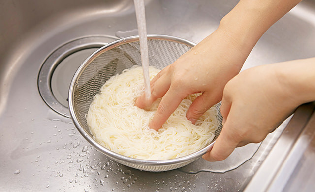 ざるに上げたそうめんを流水でもみ洗いしている写真