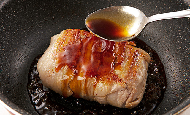 両面が焼けた肉巻きおにぎりに、スプーンで煮汁をかけている写真