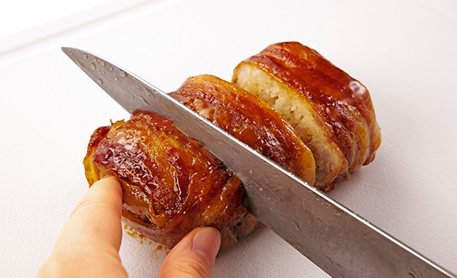 焼き上がった肉巻きおにぎりをまな板にのせ、包丁で食べやすく切っている写真