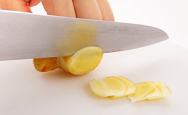 生姜を包丁で薄切りにしている写真