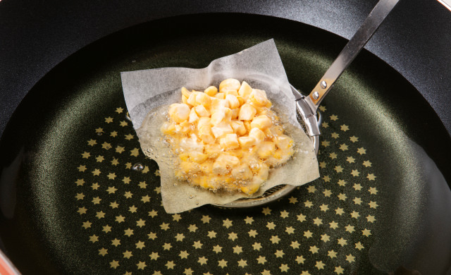 オーブンシートにのせたタネを網じゃくしにのせ、油の中に入れている写真