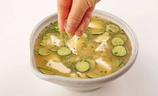 きゅうり、大葉、豆腐が入った冷や汁に仕上げとしてすりごまがかかっている写真