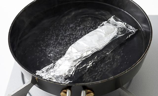 沸騰した湯の中にアルミホイルに包んだ鮭を入れてゆでている写真