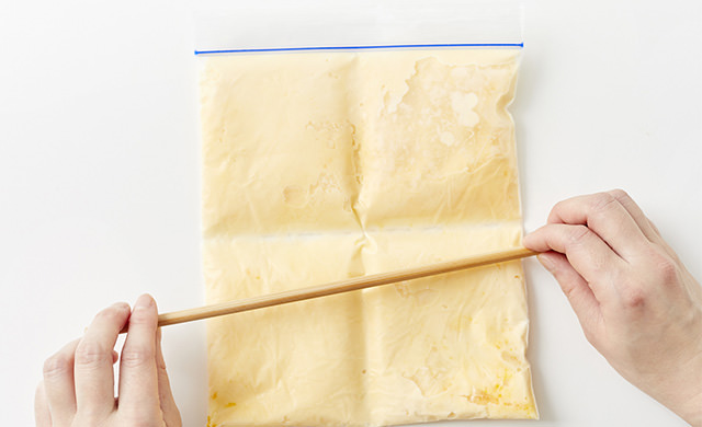 手作りアイスクリームが入った冷凍用保存袋に菜箸を当てて折れ目をつけている写真