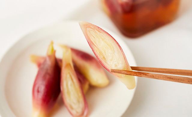 手前に甘酢漬けのみょうが、奥に瓶入りの甘酢漬けみょうが。甘酢漬けみょうがを箸で持ち上げている写真