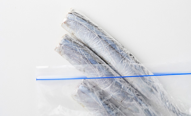 ラップに包まれて冷凍されたさんまを冷凍用保存袋から取り出している写真