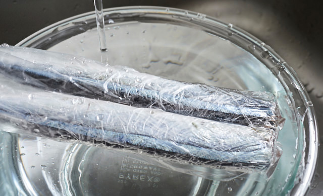 ラップに包まれて冷凍されたさんまをポリ袋に入れて流水解凍している写真