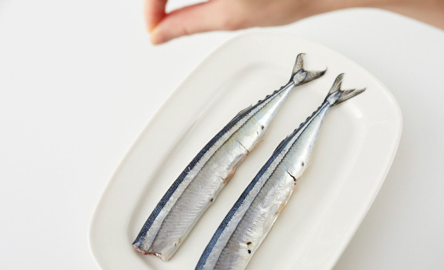 皿においたさんまに高い位置から塩を振っている写真