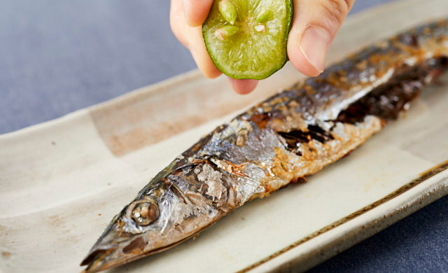 サンマの塩焼きに、カット冷凍すだちの果汁を搾っている写真