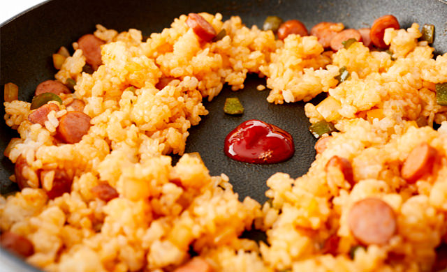 フライパンで炒めたケチャップライスの真ん中に空間を作り、そこにケチャップを入れている写真