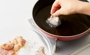 下味をつけて薄力粉をまぶした鶏もも肉に、片栗粉をまぶしながら170℃の揚げ油に入れている写真
