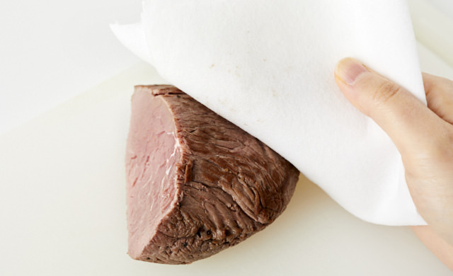 切り分けたローストビーフの表面をキッチンペーパーで拭いている写真