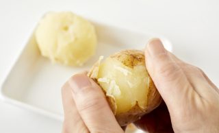 ゆでたじゃがいもの皮をむいている写真