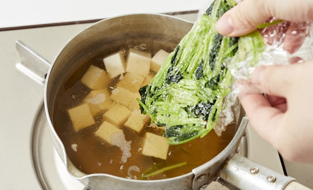 冷凍三つ葉を汁物に加えている写真