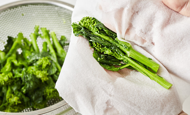 菜の花をざるにあげて、水気を拭き取る写真