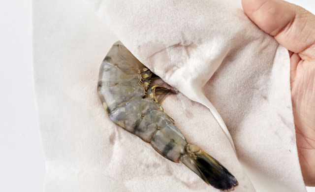 殻付きエビの水分をキッチンペーパーで拭き取る写真