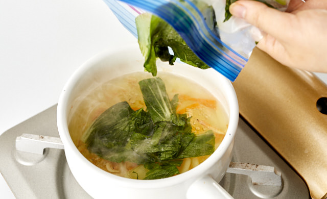 冷凍したチンゲン菜をスープに加えている写真