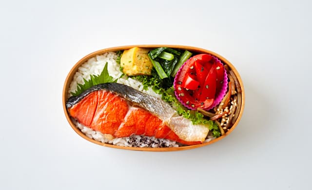 お弁当箱に焼き鮭を詰めた写真