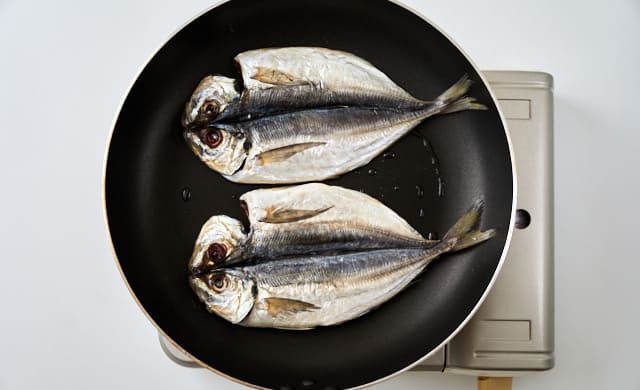 フライパンでアジの干物を焼いている写真