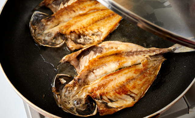 フライパンでアジの干物の皮目を下にして焼いている写真