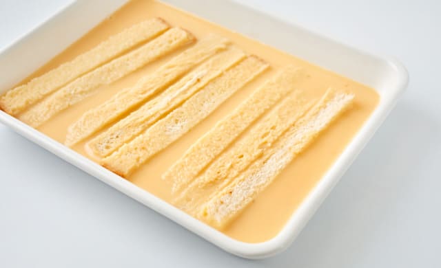 卵液を入れたバットにパンの耳を入れている写真