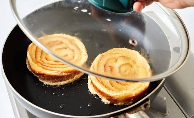 丸形のパンの耳をフライパンで蒸し焼きにしている写真