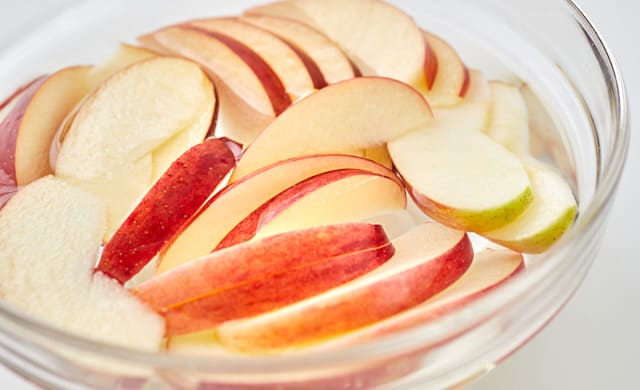 薄切りしたりんごを塩水に入れている写真