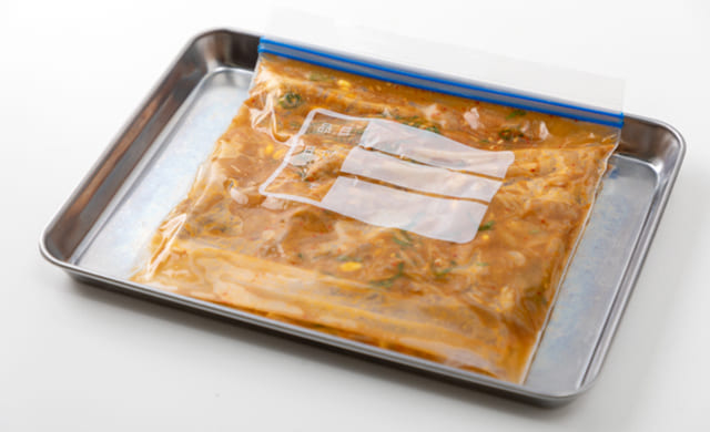 ラップで四角く包んだおかずをトレーにのせて平らに冷凍している写真