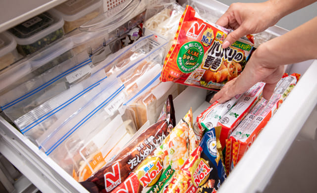 冷凍庫下段の奥に新しい冷凍食品を入れている写真