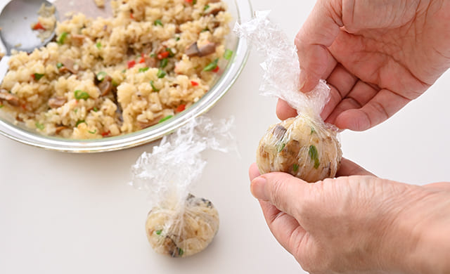 ピラフをラップで茶巾のように絞って丸いおにぎりを作っている写真