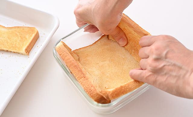 耐熱容器に食パンを敷き込んでいる写真