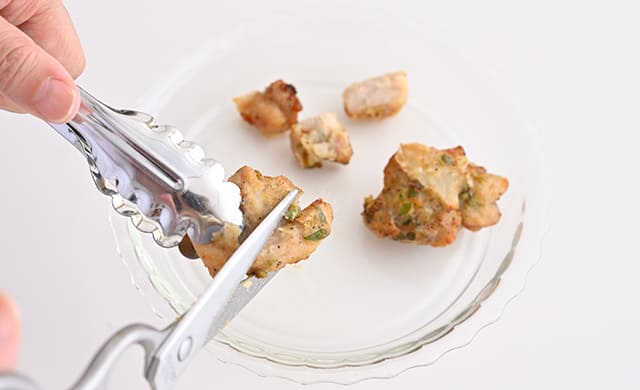 『やみつきねぎ塩焼き鳥』をキッチンばさみで一口大に切っている写真