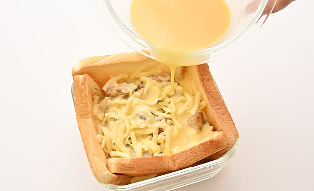食パンの上に溶けるチーズをのせ、卵液を流し込んでいる写真