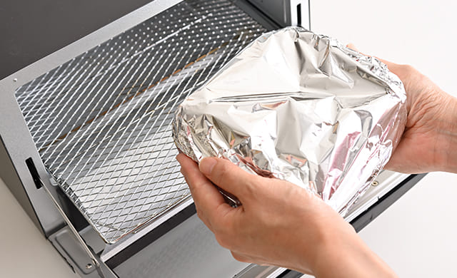 アルミホイルをかぶせた耐熱容器をトースターに入れようとしている写真