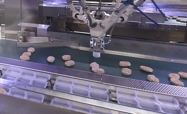 アームロボットがトレイに『ミニハンバーグ』を入れている写真