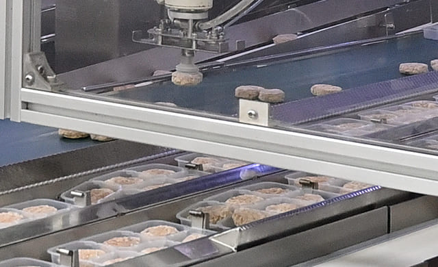 アームロボットがトレイに『ミニハンバーグ』を入れている写真