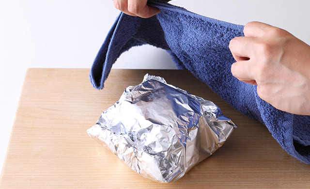アルミホイルで包んだ肉をタオルで覆っている写真