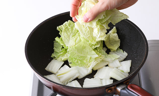 白菜の芯を炒めたところに葉を加えている写真