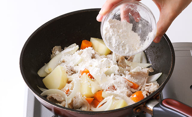炒めた具材に小麦粉を振り入れている写真