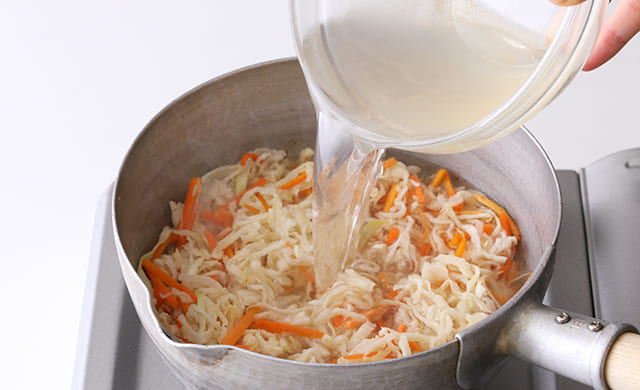 炒めた切り干し大根とにんじんにだし汁を加えている写真