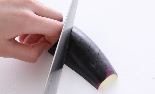 半分に切ったなすの皮目に斜めの切り込みを入れている写真