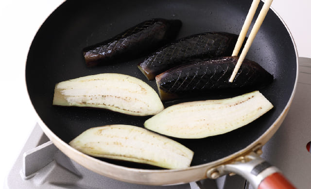 なすを裏返し、焼き色を確認している写真